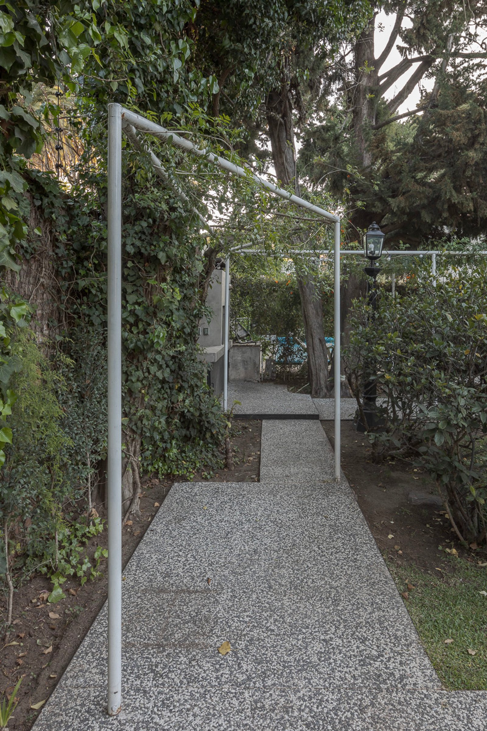 Sendero de piedra y pérgola entre la vegetación frondosa — proyecto Jardines Catamarca, por Estudio YME, en B1636 Olivos